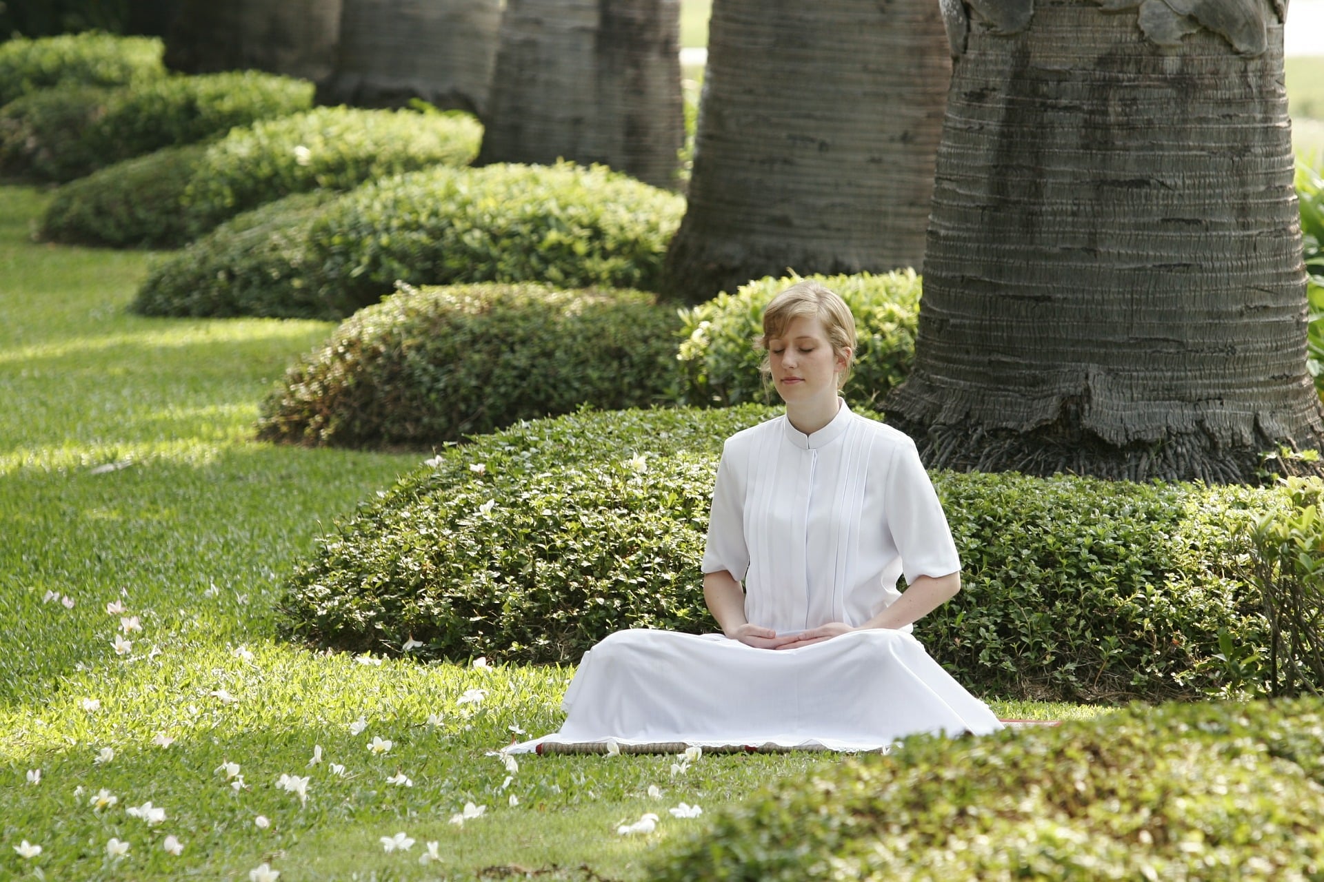 A woman in white dress is meditating in a garden