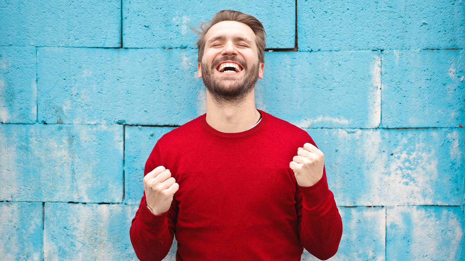 a man in red shirt standing in front of blue wall, expressing happiness