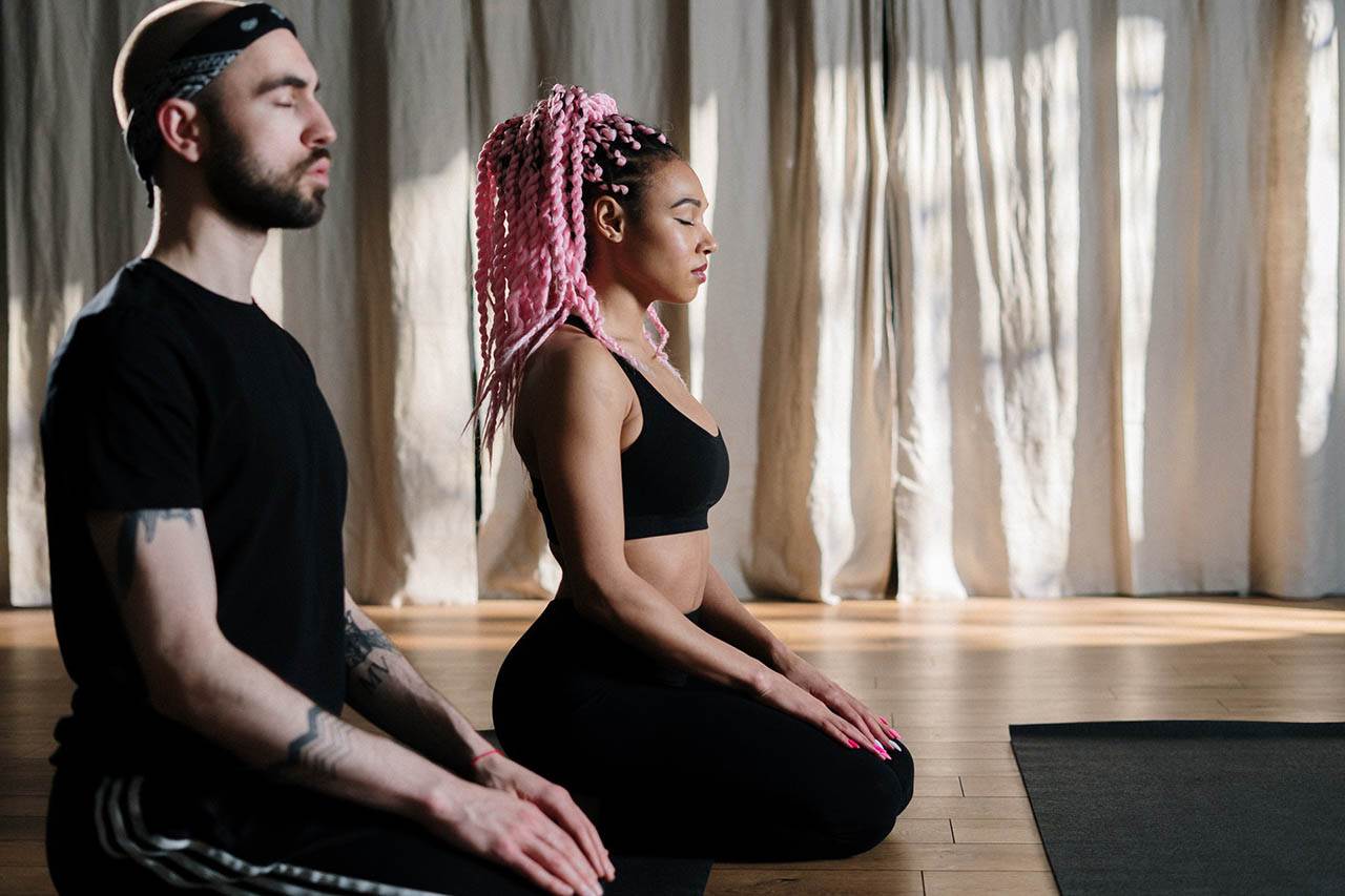 practicing meditation with the right attitude, a man and a woman sitting side by side on the floor with their eyes closed.